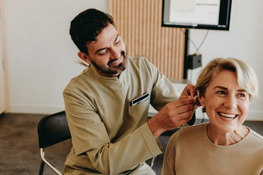An audiologist fitting a discreet hearing aid behind the ear of a smiling older woman