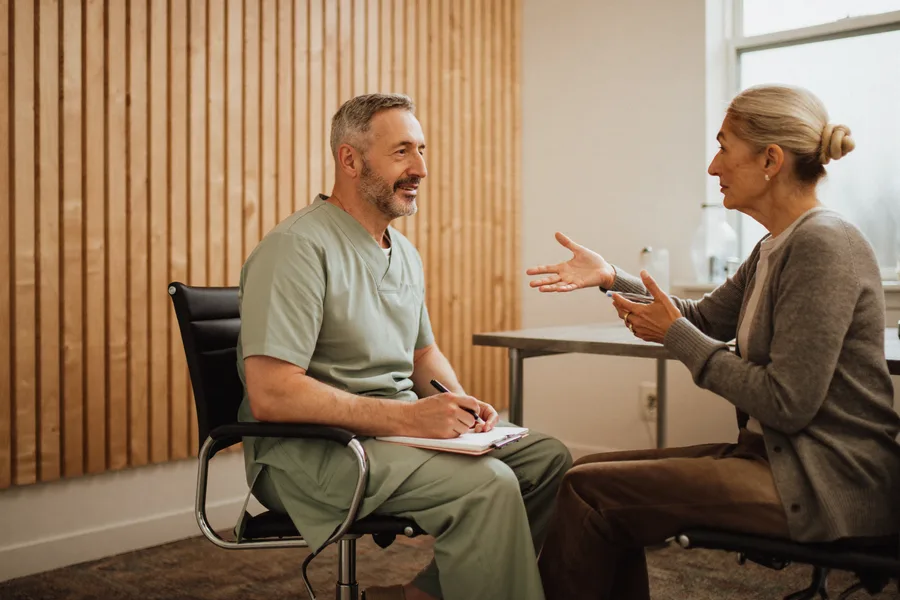 An audiologist listening and taking notes as an older patient describes her hearing difficulties