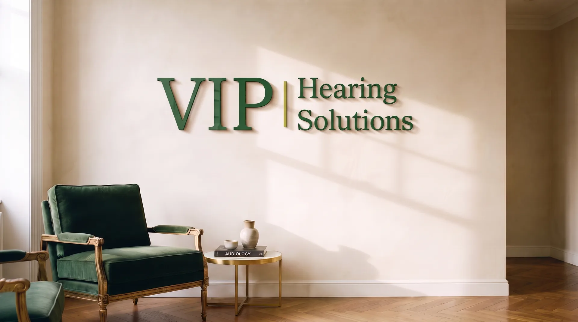 The practice waiting room: a dark green velvet armchair beside a brass table holding a book titled Audiology, against a warm plaster wall in soft window light