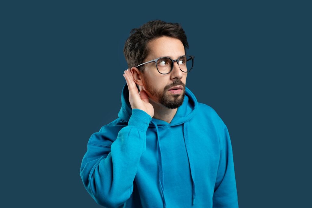 man wearing a blue hoodie and eyeglasses having difficulty hearing