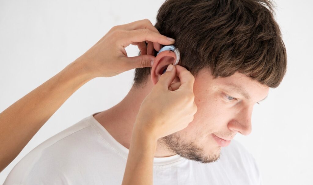person helping a man wear a hearing aid