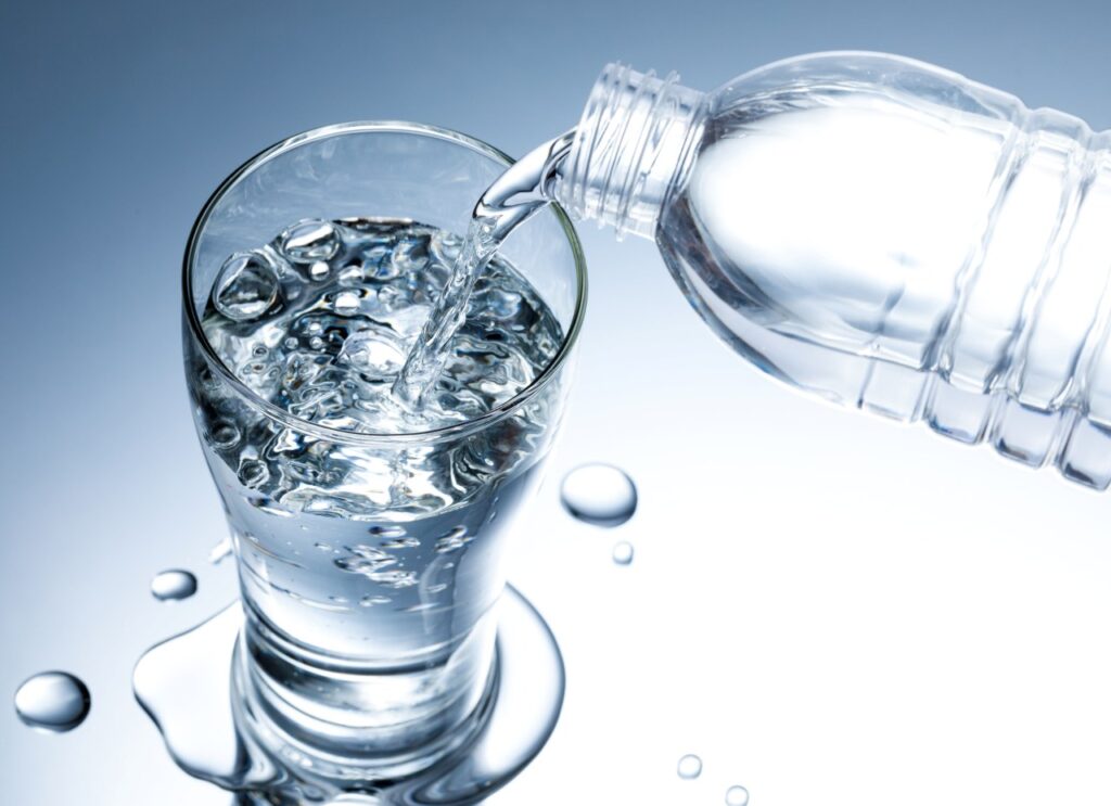 Pouring fresh pure water from bottle into a glass on the table with water droplets