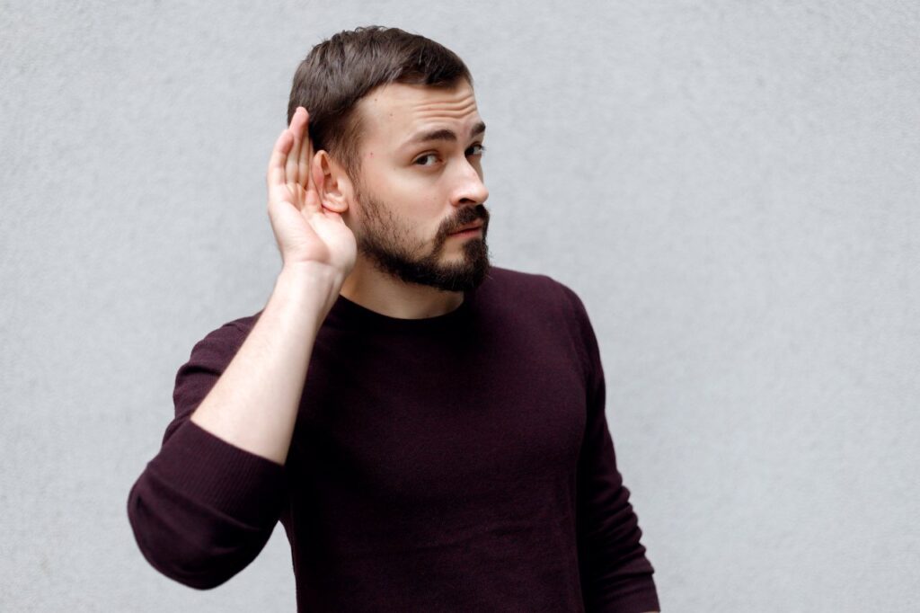 man with beard with his hand against his ear having trouble with hearing