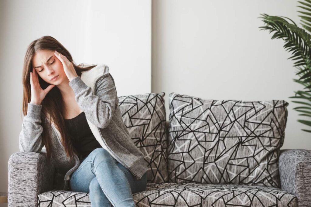 woman experiencing headache while sitting on a grey sofa