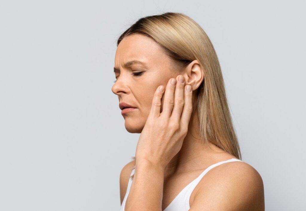 woman touching her ear with a worried look on her face