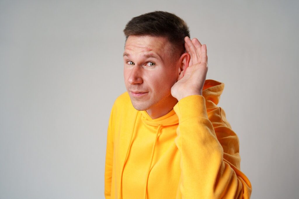 man wearing yellow hoodie with his hand on his ear