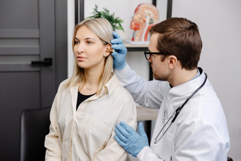 Otolaryngologist doctor checking young woman's ear using otoscope or auriscope at ENT clinic