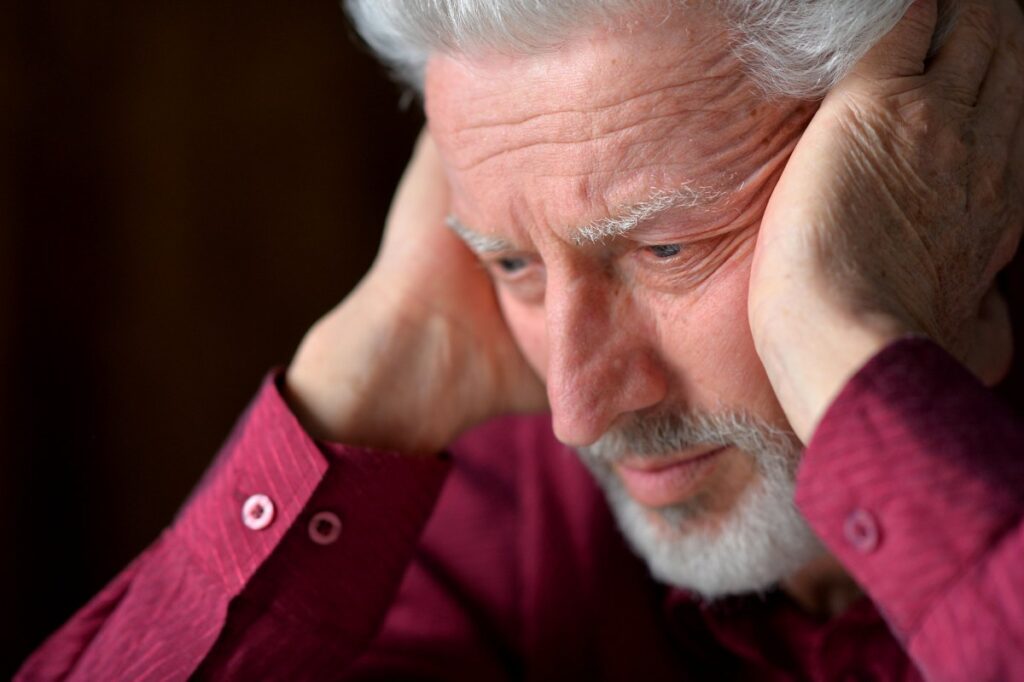 elderly man with his hands on his ears