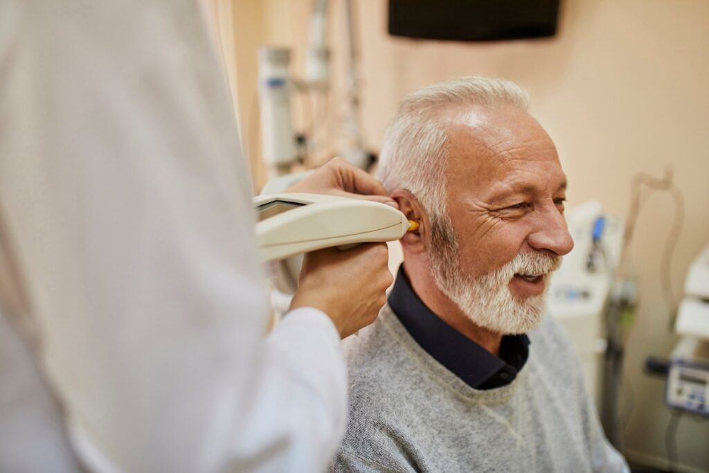 elderly man smiling while having his ear checked by a medical professional