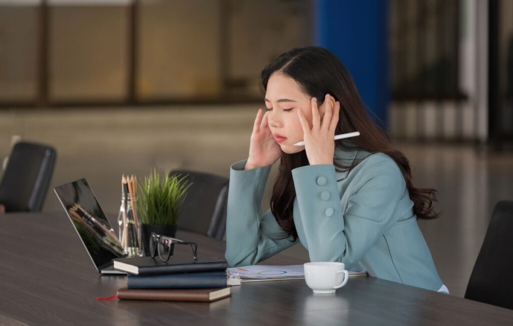 asian woman with headache looking uncomfortable while working