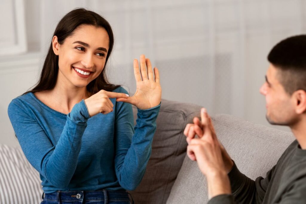 Smiling deaf and mute couple communicating at home using sign language, sitting on couch in living room