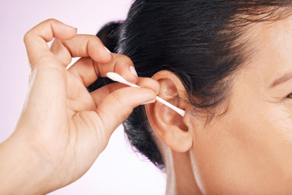 Woman, cotton and cleaning ear in studio in cropped closeup for wellness by pink background