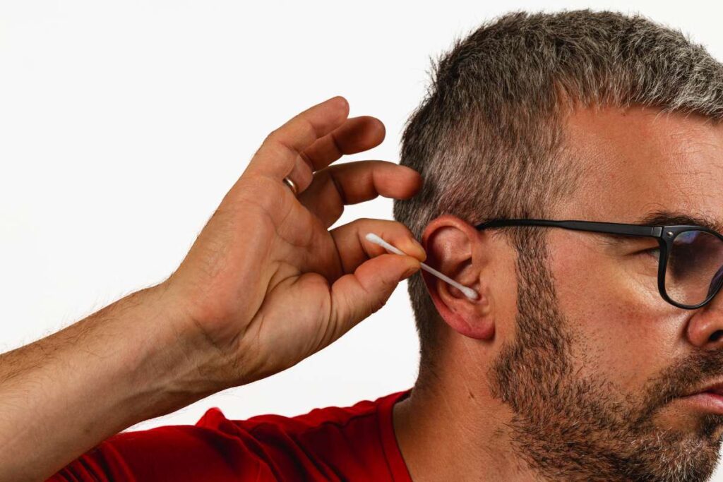Man cleaning ear with cotton swab in home setting during daytime